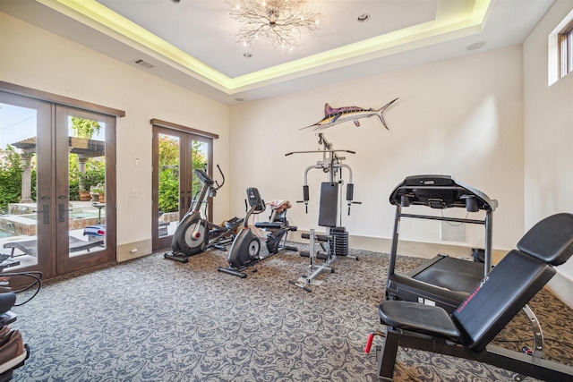 workout room featuring a tray ceiling, carpet floors, and french doors