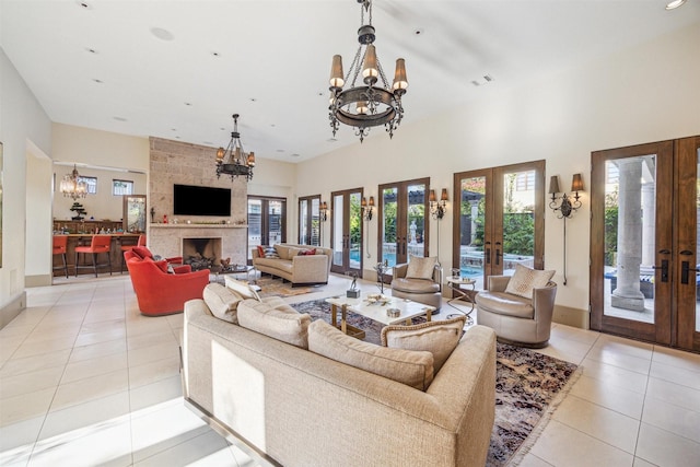 tiled living room with a towering ceiling, a fireplace, an inviting chandelier, and french doors