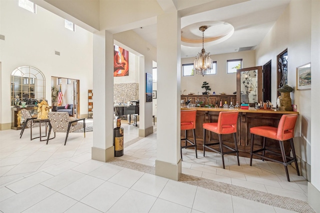 bar featuring an inviting chandelier, pendant lighting, a raised ceiling, and light tile patterned floors