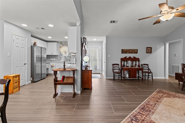 kitchen featuring tasteful backsplash, a textured ceiling, ceiling fan, white cabinetry, and stainless steel refrigerator