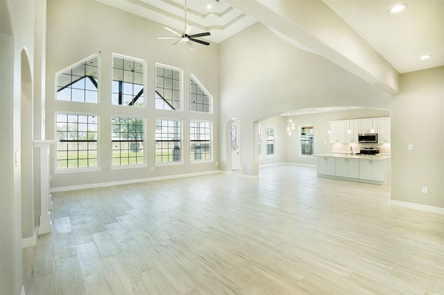 1714 Mackey Dr, Dickinson, TX 77539 - unfurnished living room featuring a ceiling fan, arched walkways, baseboards, light wood-type flooring, and a towering ceiling