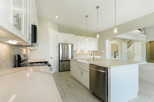 kitchen with a center island with sink, appliances with stainless steel finishes, sink, white cabinetry, and hanging light fixtures