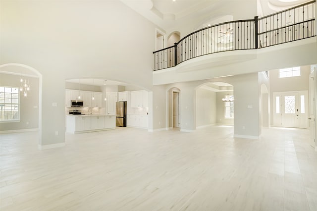 unfurnished living room featuring an inviting chandelier, a high ceiling, and light hardwood / wood-style flooring