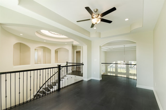 corridor featuring a tray ceiling, dark wood-type flooring, and a notable chandelier