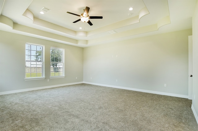 carpeted spare room with a raised ceiling and ceiling fan