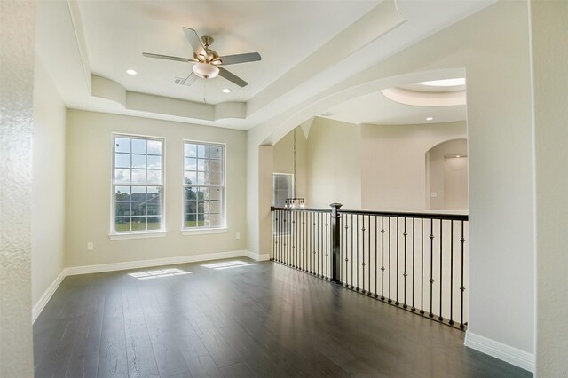 empty room featuring a tray ceiling, ceiling fan, and dark hardwood / wood-style flooring