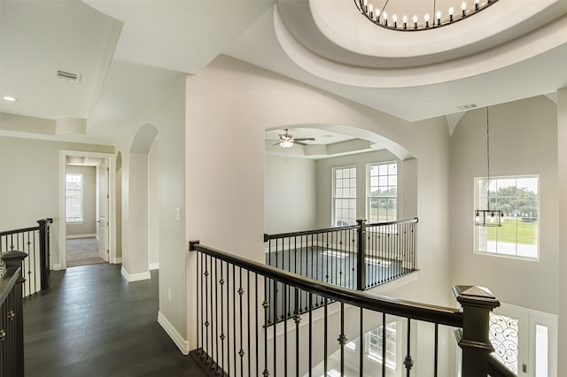 corridor with a tray ceiling, plenty of natural light, dark wood-type flooring, and a notable chandelier