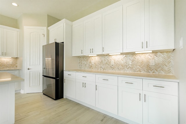 kitchen featuring stainless steel fridge, light hardwood / wood-style flooring, white cabinetry, and tasteful backsplash