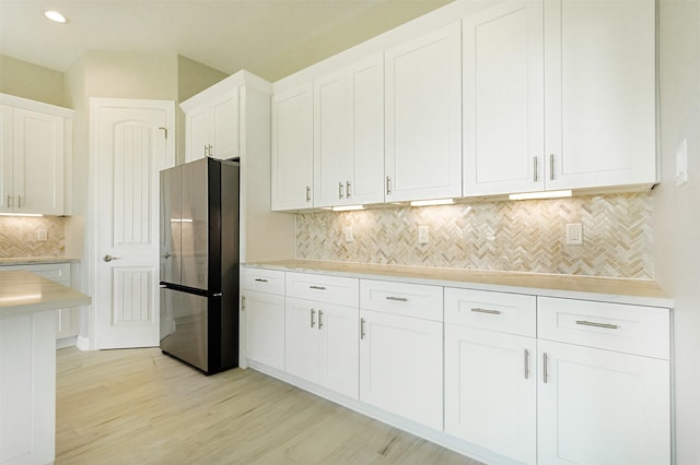 1714 Mackey Dr, Dickinson, TX 77539 - kitchen featuring freestanding refrigerator, decorative backsplash, white cabinets, light wood-type flooring, and light countertops