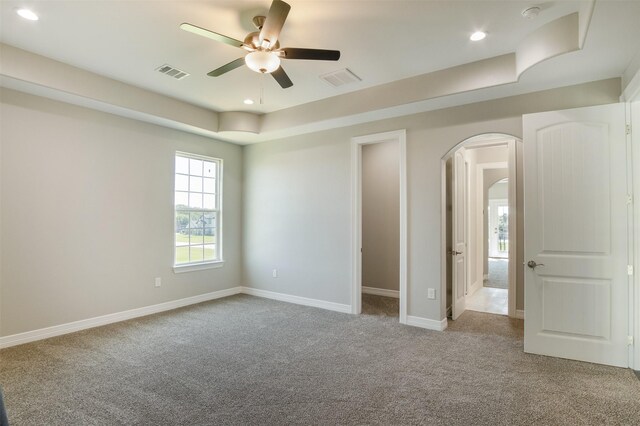 spare room with a raised ceiling, ceiling fan, and light colored carpet