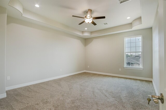 carpeted empty room with ceiling fan and a raised ceiling