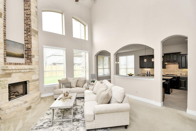 carpeted living room featuring a stone fireplace and a high ceiling