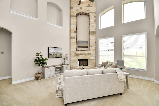 carpeted living room with ceiling fan, a stone fireplace, and a towering ceiling