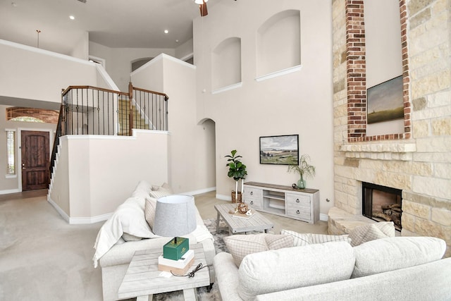 carpeted living room featuring a stone fireplace, ceiling fan, and a towering ceiling