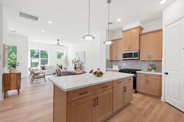 kitchen featuring ceiling fan, hanging light fixtures, light hardwood / wood-style floors, decorative backsplash, and appliances with stainless steel finishes