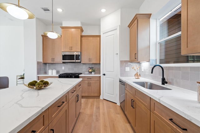 kitchen with appliances with stainless steel finishes, light wood-type flooring, backsplash, sink, and decorative light fixtures