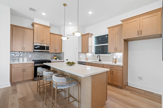 kitchen featuring hanging light fixtures, sink, light hardwood / wood-style flooring, appliances with stainless steel finishes, and a kitchen island