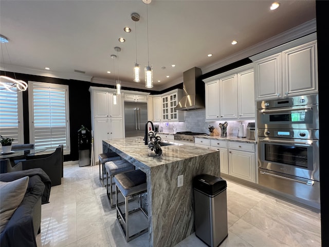 kitchen with stainless steel appliances, pendant lighting, wall chimney range hood, and white cabinets