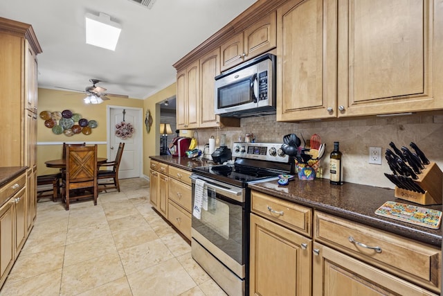 kitchen featuring dark stone counters, light tile patterned floors, ceiling fan, stainless steel appliances, and decorative backsplash