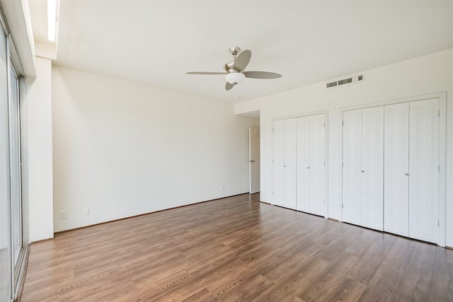 unfurnished bedroom featuring hardwood / wood-style flooring, multiple closets, and ceiling fan