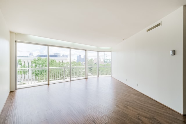 empty room with a wealth of natural light, wood-type flooring, and expansive windows