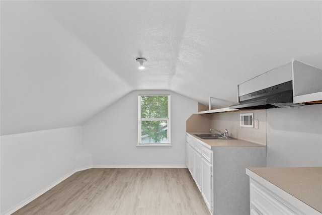 interior space featuring sink, light hardwood / wood-style flooring, white cabinetry, a textured ceiling, and vaulted ceiling