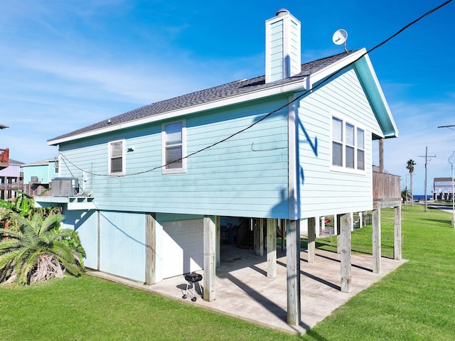 back of house with roof with shingles, a lawn, a chimney, a carport, and an attached garage