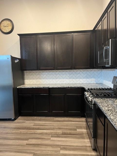 kitchen with backsplash, light stone countertops, light wood-type flooring, dark brown cabinetry, and stainless steel appliances