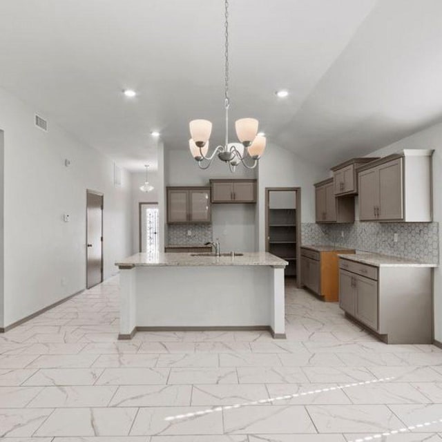 kitchen featuring sink, light stone counters, hanging light fixtures, an island with sink, and a notable chandelier