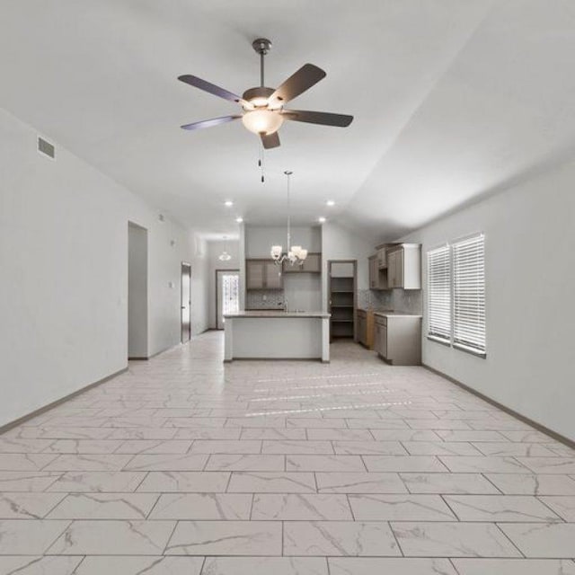 unfurnished living room featuring lofted ceiling, ceiling fan with notable chandelier, and a wealth of natural light