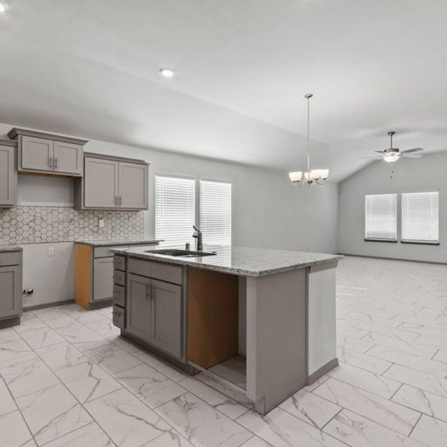 kitchen with sink, gray cabinetry, an island with sink, decorative light fixtures, and vaulted ceiling