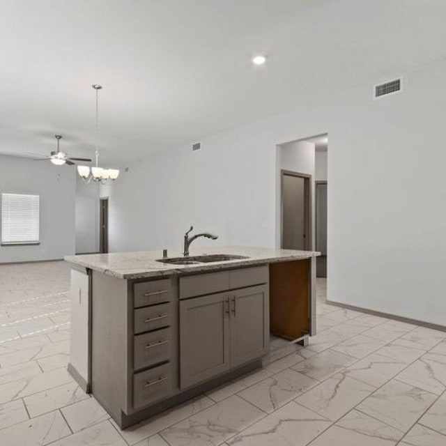 kitchen featuring sink, light stone counters, a kitchen island with sink, pendant lighting, and ceiling fan with notable chandelier