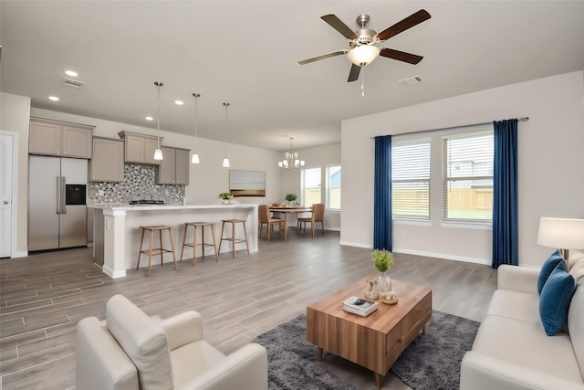 living room with visible vents, wood finished floors, and ceiling fan with notable chandelier