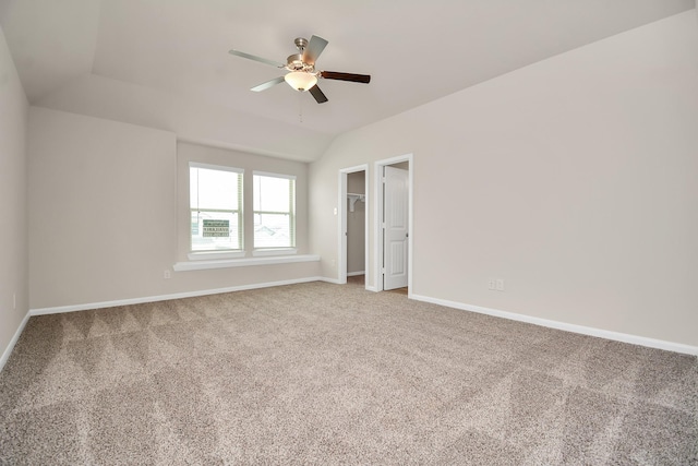 unfurnished bedroom featuring lofted ceiling, ceiling fan, baseboards, carpet, and a walk in closet