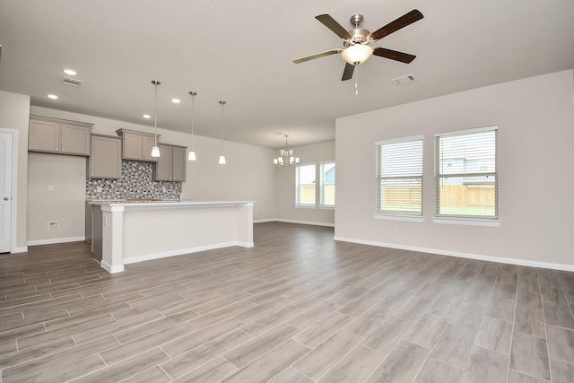 unfurnished living room featuring recessed lighting, ceiling fan with notable chandelier, visible vents, baseboards, and light wood-type flooring