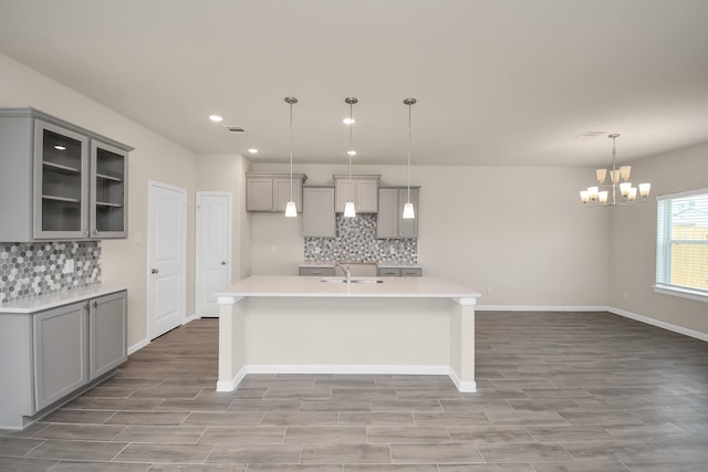 kitchen with an island with sink, glass insert cabinets, light countertops, and gray cabinetry