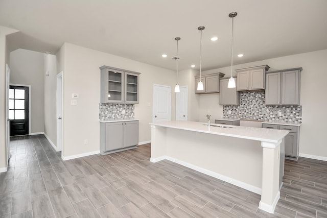 kitchen with glass insert cabinets, light countertops, a sink, and gray cabinetry