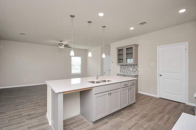 kitchen with a sink, visible vents, light countertops, an island with sink, and glass insert cabinets