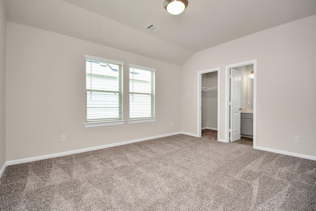 unfurnished bedroom with visible vents, baseboards, vaulted ceiling, a spacious closet, and carpet