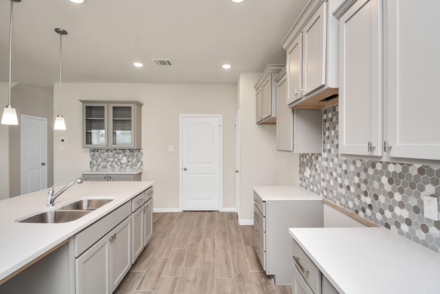 kitchen featuring glass insert cabinets, hanging light fixtures, gray cabinets, light countertops, and a sink