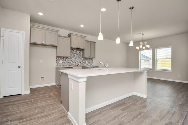 kitchen with decorative backsplash, an island with sink, decorative light fixtures, wood tiled floor, and light countertops