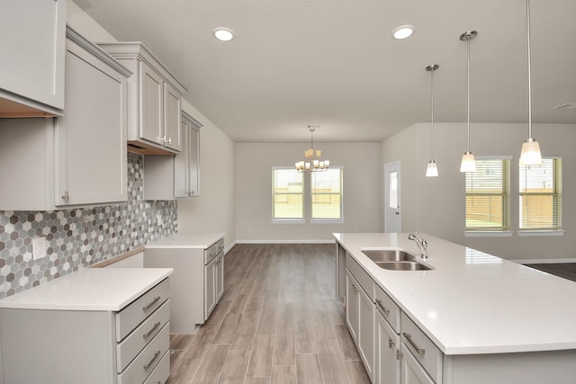 kitchen with an island with sink, gray cabinets, a sink, and pendant lighting