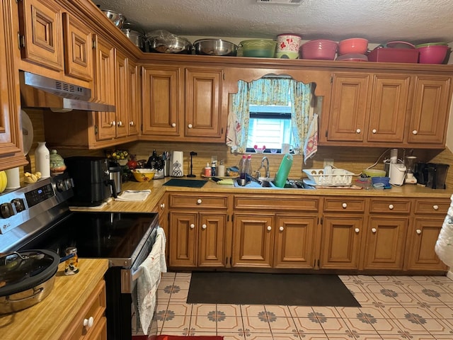 kitchen featuring stainless steel electric stove, wall chimney exhaust hood, sink, a textured ceiling, and light tile patterned flooring