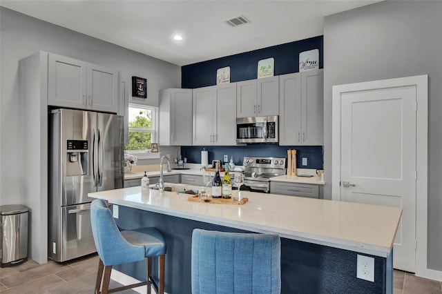 kitchen with appliances with stainless steel finishes, light wood-type flooring, a breakfast bar, sink, and an island with sink