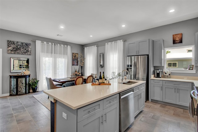 kitchen with gray cabinets, sink, stainless steel appliances, and a kitchen island with sink