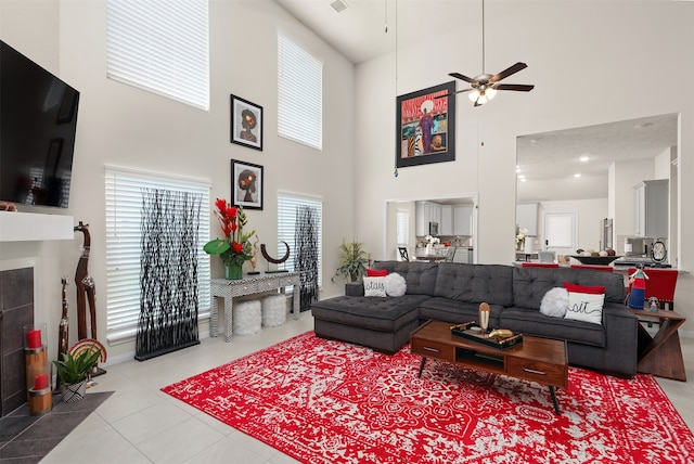 tiled living room featuring a tiled fireplace, ceiling fan, and a high ceiling