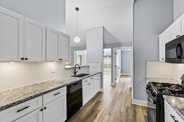 kitchen with light stone countertops, white cabinetry, hanging light fixtures, dark hardwood / wood-style flooring, and black appliances