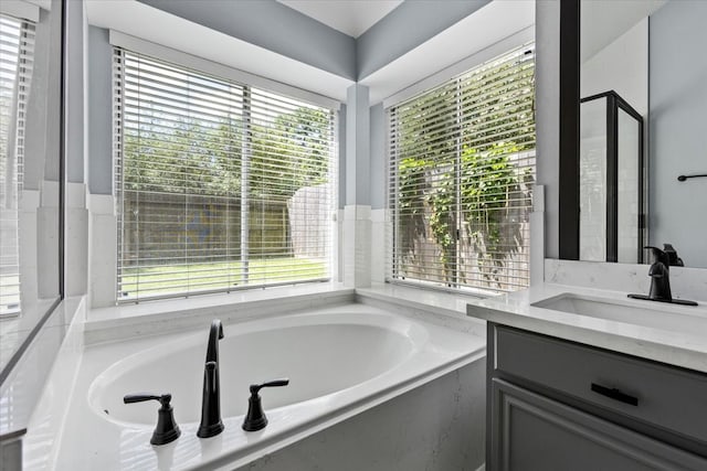 bathroom with vanity, a relaxing tiled tub, and a healthy amount of sunlight