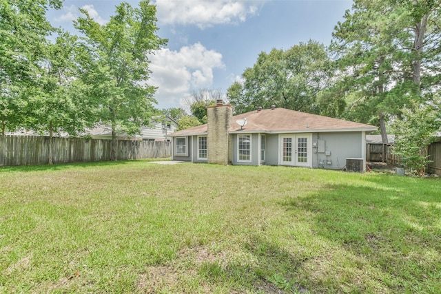 rear view of house with central AC, a chimney, a fenced backyard, and a lawn