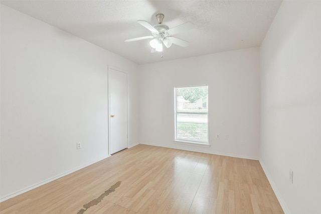 spare room featuring ceiling fan, light wood-style flooring, baseboards, and a textured ceiling